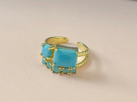Gold adjustable ring with large emerald-cut center stone, round turquoise accent, and five teardrop details. Sizes: adjustable.