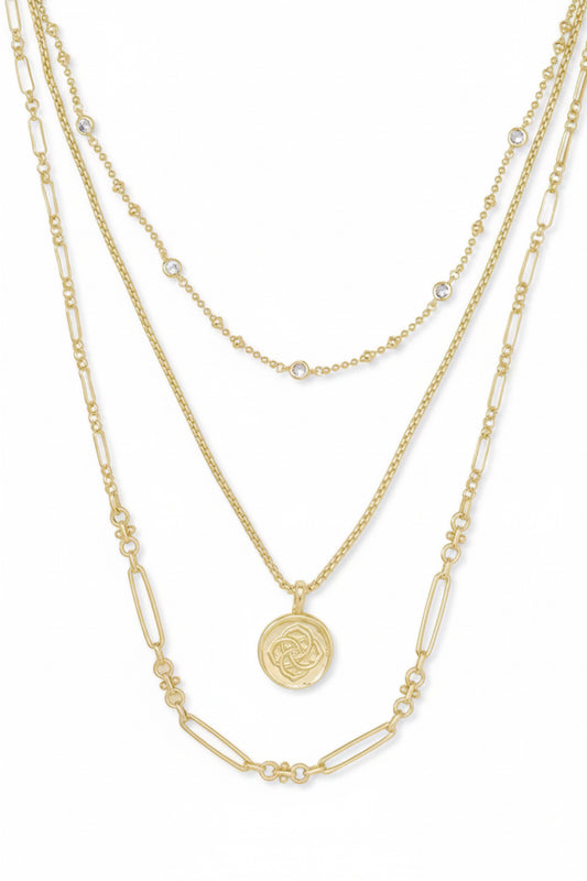 The Gold Medallion Coin Kendra Scott Necklace is a four-layered gold-plated brass necklace with oval links and beads, small gem accents, an engraved medallion coin pendant, and larger elongated links. Available in standard necklace sizes.