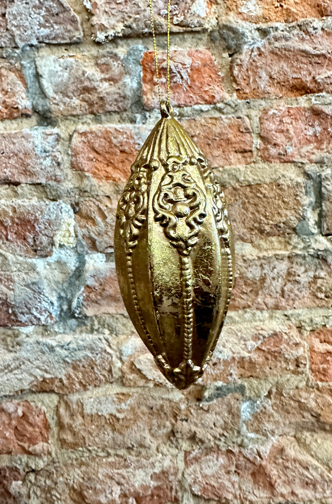 Gold elongated oval ornament with embossed patterns on a gold string.