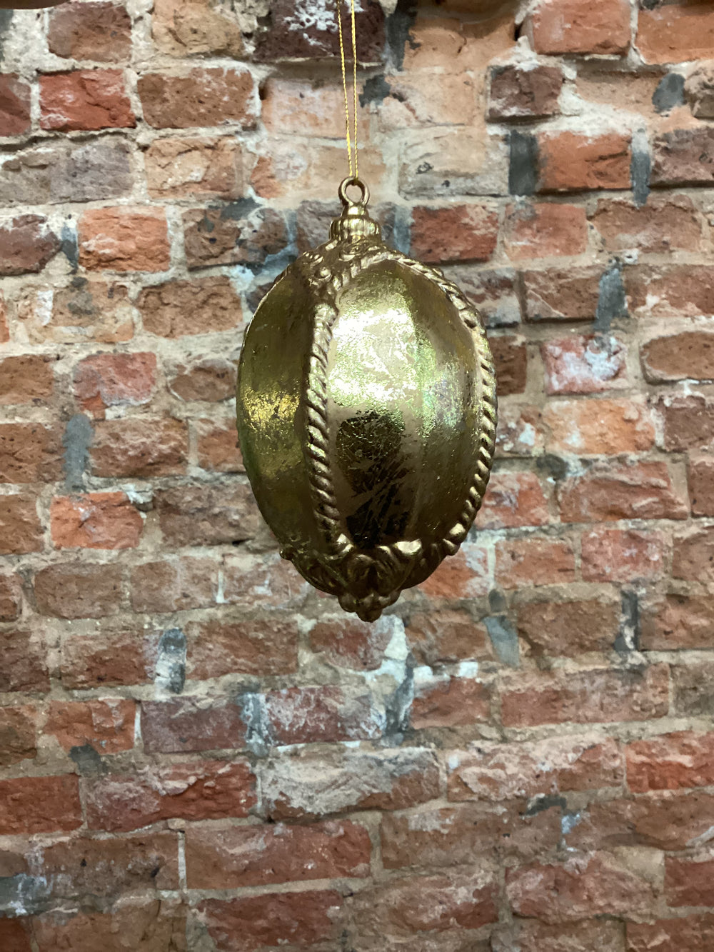 Gold elongated oval ornament with embossed scroll and rope detailing.