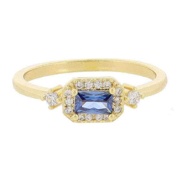 This product is an 18K Gold Plated ring adorned with Mini Crystal Outline and Side Crystals. It boasts a stunning central blue gemstone encircled by smaller diamonds. More diamonds are set on the band for added brilliance. Available sizes for the ring vary.