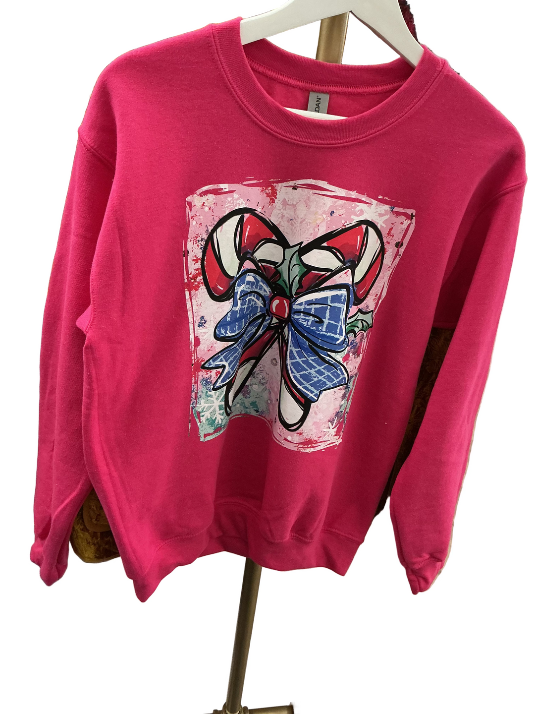Bright pink Christmas sweatshirt with crossed candy canes, blue plaid bow, and holly leaves. Available in various sizes.