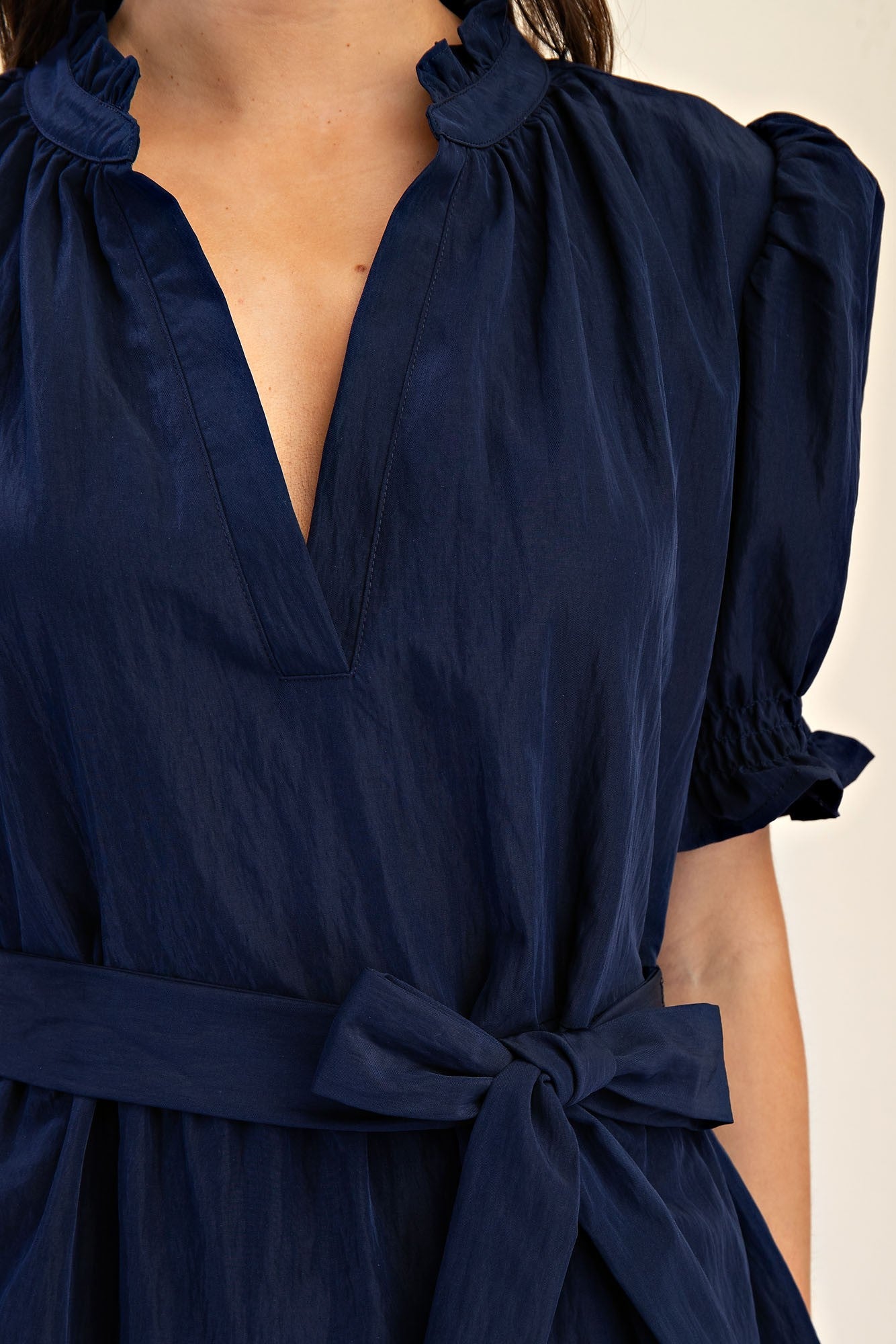 Mavis Navy Ruffle Neck Dress with puff sleeves, ruffled V-neck, tie-waist bow. Subtle sheen. Available in sizes XS-XL.