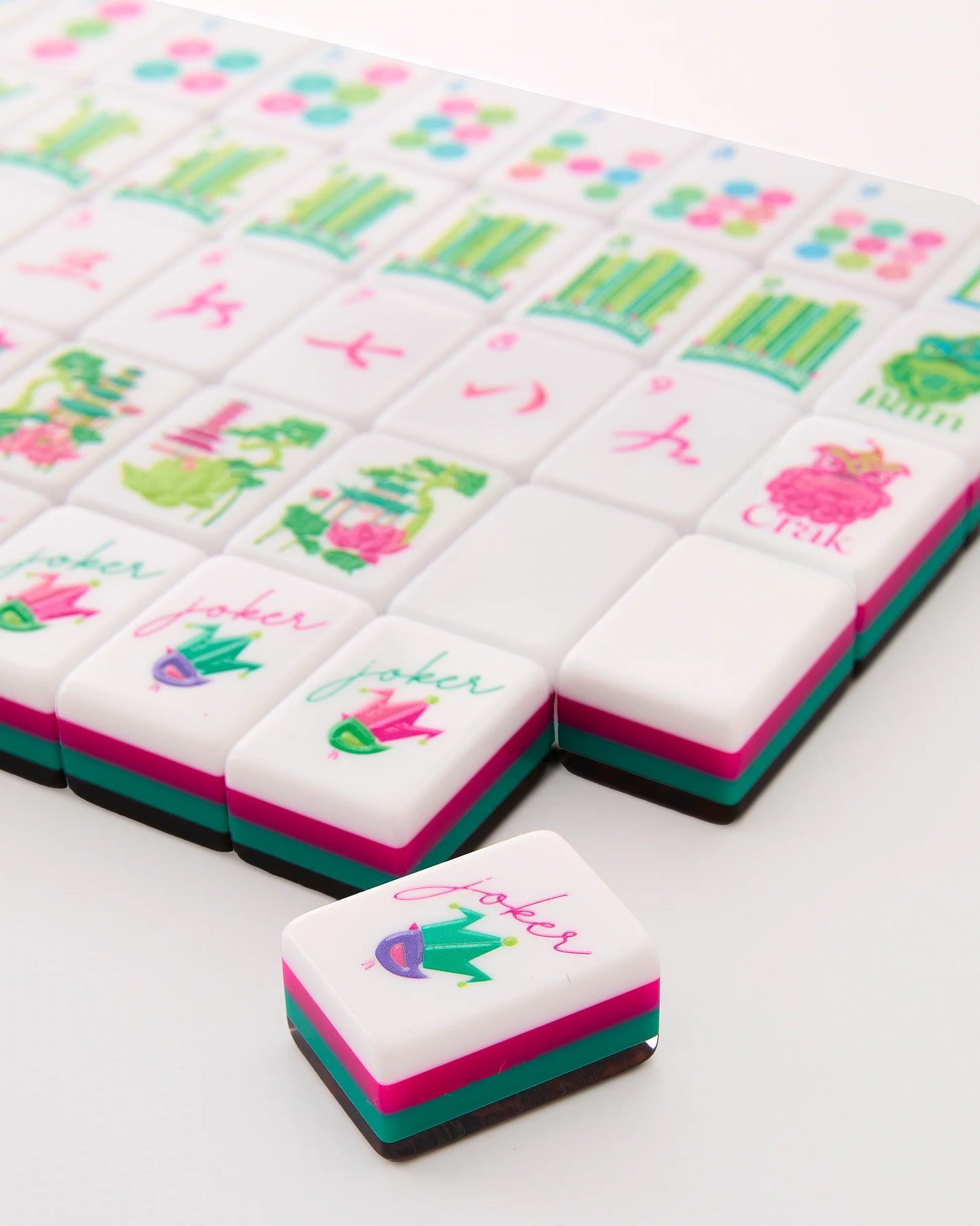 Glow Wild Mahjong Tiles with modern designs in pink, green, and blue accents; "joker" tile featured. Available in standard and travel sizes.