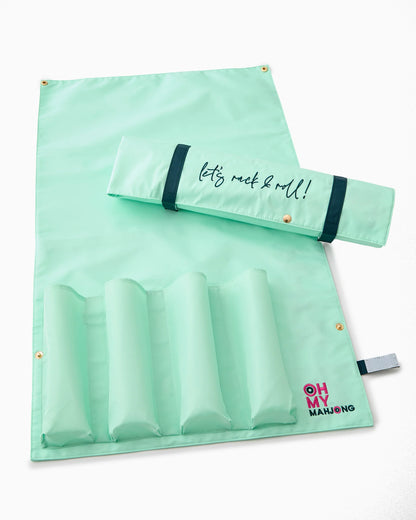 Mint-green roll-up bag with four padded sections, a flap reading "let’s rock & roll!", and a small “OH MY MAHJONG” logo in pink and red at the corner. Sizes available: standard.