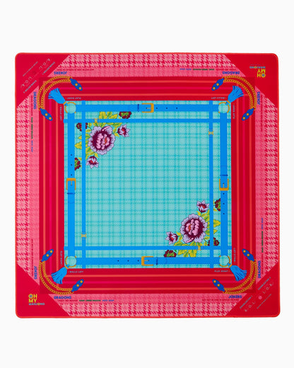 The Penelope Mat in Tube has a square design with a red and pink houndstooth border, blue plaid center, floral accents, and yellow and blue geometric lines. Available sizes: small, medium, large.