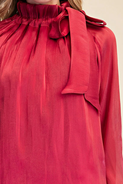 Close-up of the red Ruffle Neck Adjustable Tie Long Sleeve Blouse with a silky finish, high ruffled neckline, and adjustable tie detail on the shoulder. Available in sizes XS–XL.