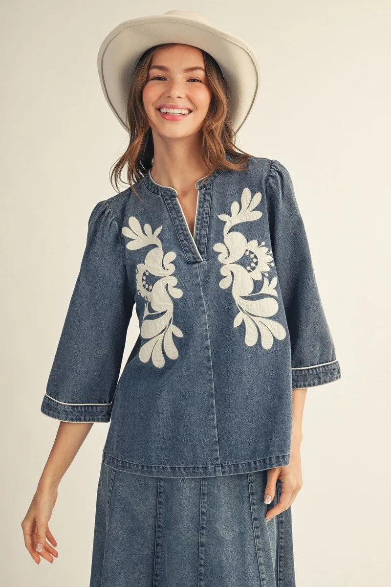 EllienWashed Denim Floral Top with white floral embroidery and 3/4 sleeves; available in sizes XS–XL.