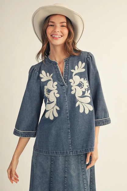 EllienWashed Denim Floral Top with white floral embroidery and 3/4 sleeves; available in sizes XS–XL.