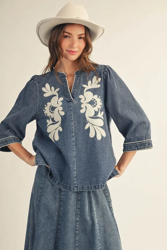 EllienWashed Denim Floral Top in washed denim with 3/4 sleeves and white floral embroidery; available in sizes XS-XL.