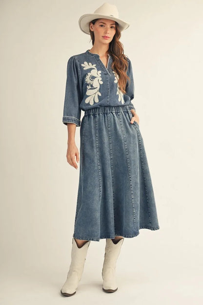EllienWashed Denim Floral Top with 3/4 sleeves, washed denim finish, and white floral embroidery. Available in sizes XS-XL.