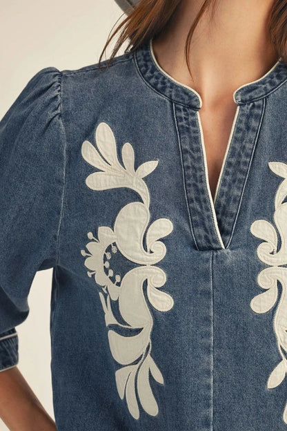 EllienWashed Denim Floral Top in blue washed denim with 3/4 sleeves, notched neckline, and white floral embroidery on the front. Available in sizes S-XL.