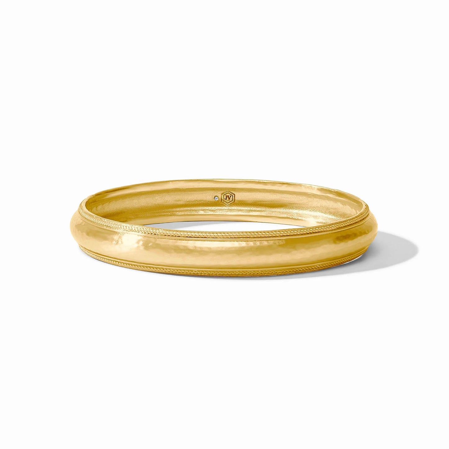 The Cannes Bangle is a shiny, polished Julie Vos bracelet with a slightly domed surface and subtle textured edge detailing in luxurious 24K gold plate. Available sizes: small, medium, large.