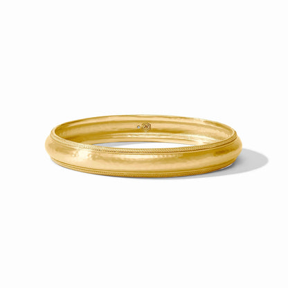The Cannes Bangle is a shiny, polished Julie Vos bracelet with a slightly domed surface and subtle textured edge detailing in luxurious 24K gold plate. Available sizes: small, medium, large.