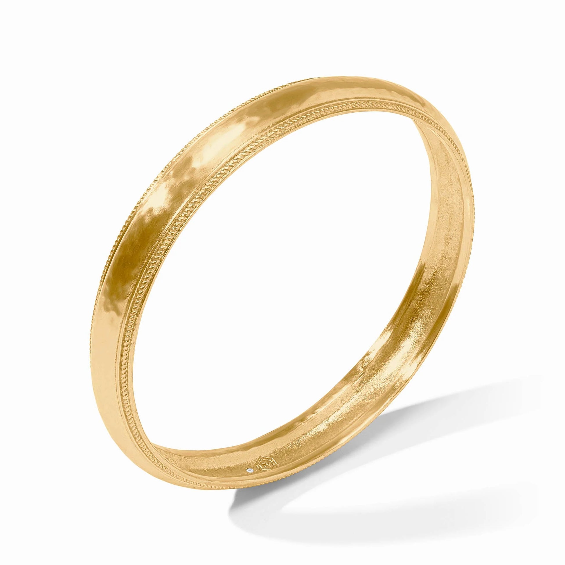 The Cannes Bangle by Julie Vos features a smooth, polished surface with a subtle decorative edge and a 24K gold plate finish. Available in standard and petite sizes.