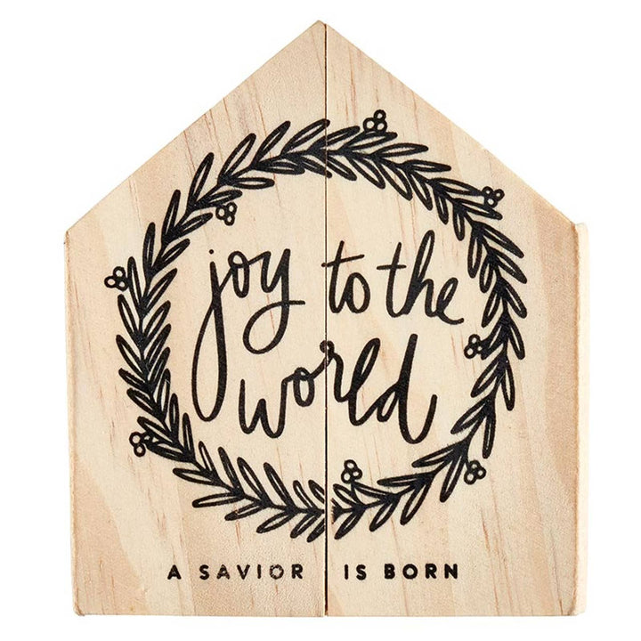 House-shaped wooden “Joy to the World” sign featuring a leaf wreath surrounding the text “A SAVIOR IS BORN.”