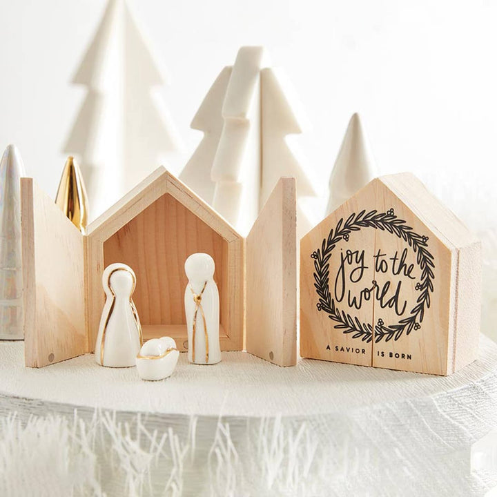 Wooden house-shaped Santa Barbara Holy Family creche with white and gold figurines and “Joy to the world, a Savior is born” text.