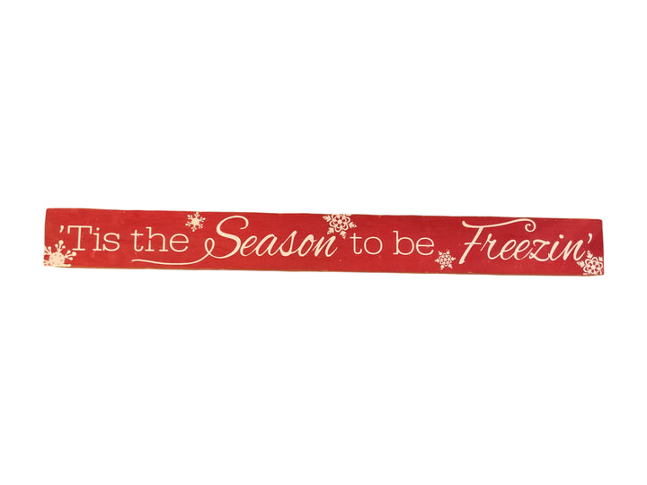 Long, rectangular red wood Christmas sign with white snowflake accents and the text, “‘Tis the Season to be Freezin’.”.