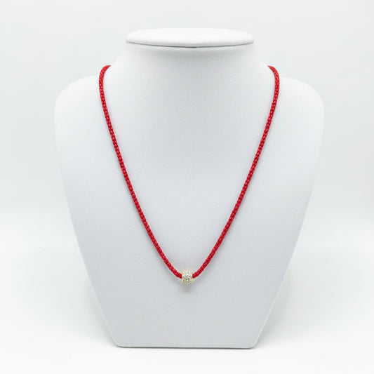 The Cassie Red Necklace has a vibrant red snake chain, a small cylindrical pendant with gold and gem accents. Available in multiple sizes.