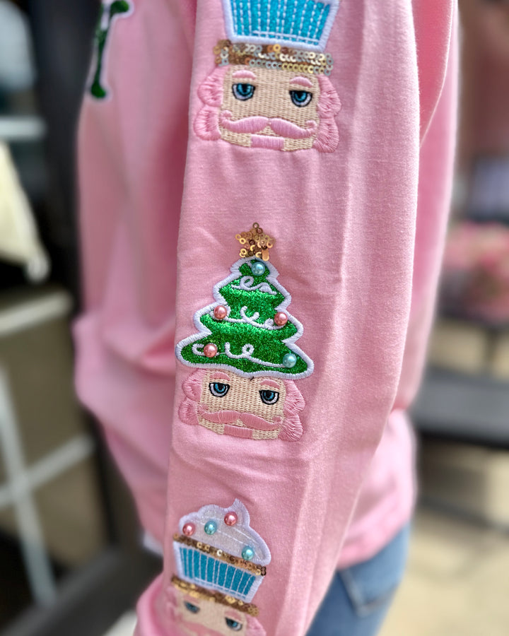 Holly Jolly Sweatshirt with pink sequin sleeves and embroidered nutcracker, Christmas tree, and cupcake. Available in sizes S-XL.