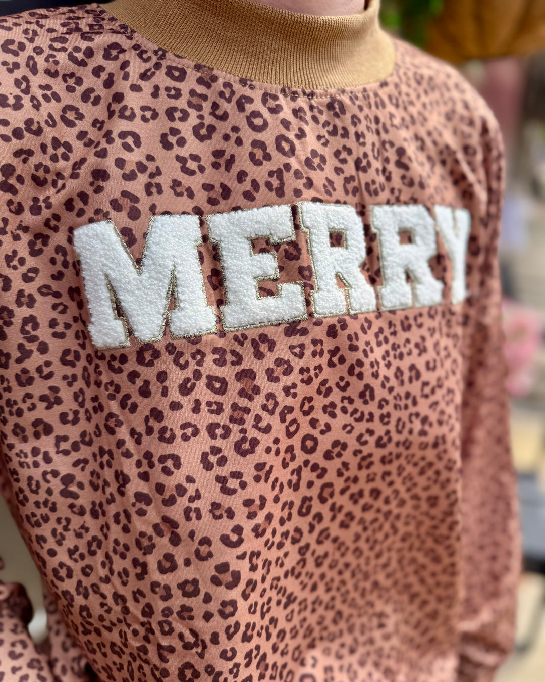 Brown leopard print mock neck sweater with “MERRY” in large white letters; available in sizes XS–XL.