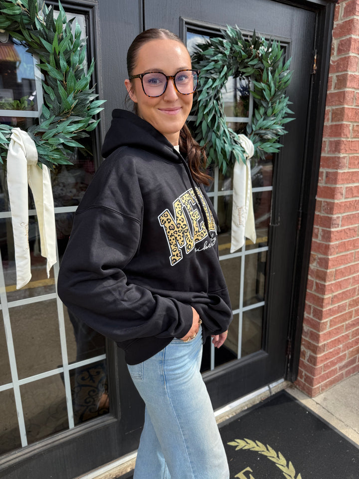 Merry Vibes Santa Hoodie: black hooded sweatshirt with “Merry Vibes Only” in leopard-print lettering. Sizes available.