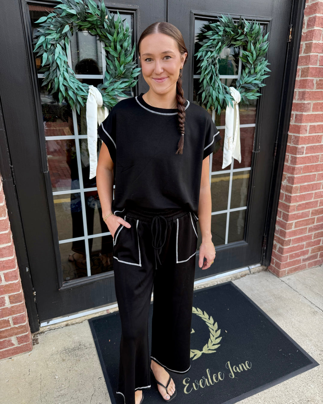 Black scuba lounge set with short-sleeve top, wide-leg pants, white contrast stitching, and drawstring waist. Available in various sizes.