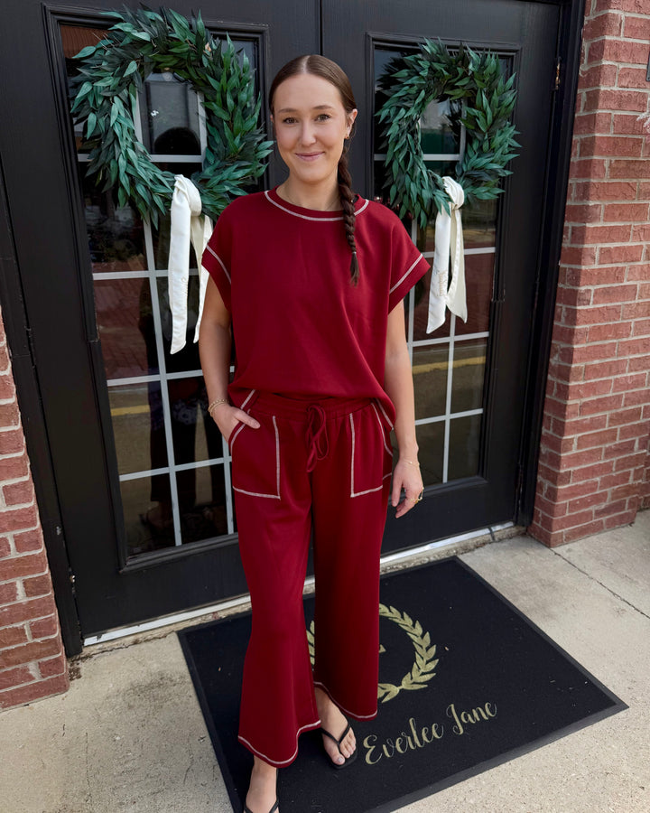 Maroon scuba lounge set with white contrast stitching, short-sleeved top, and wide-leg drawstring pants. Available in various sizes.