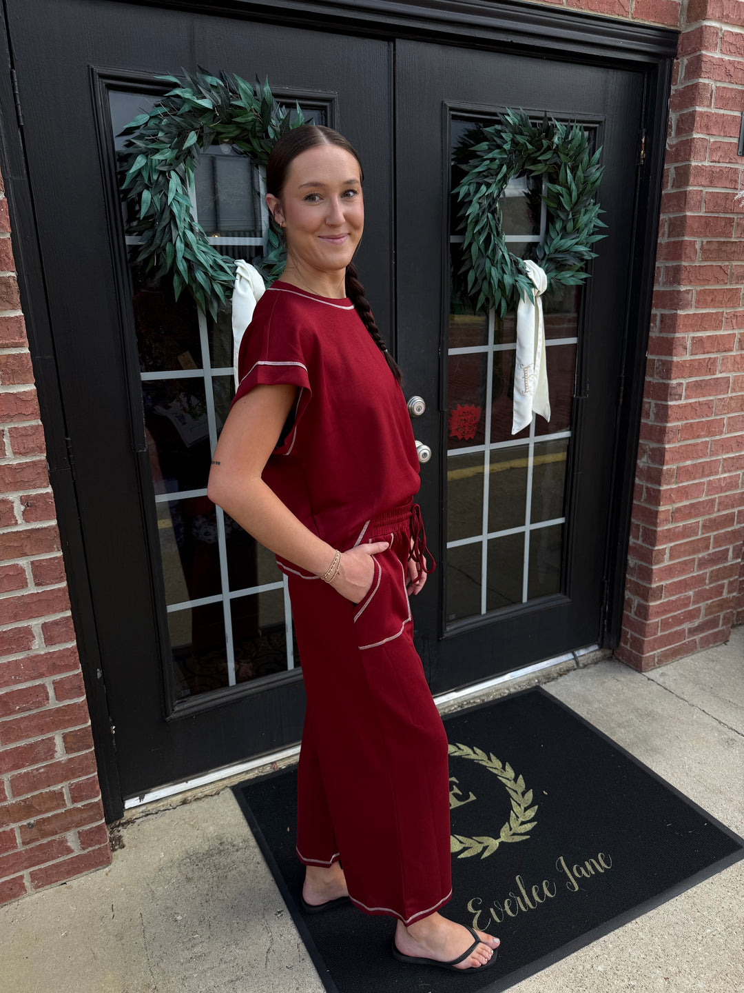 Deep red scuba lounge set with short-sleeved top, wide-leg trousers, white contrast stitching, and drawstring waist. Available in all sizes.