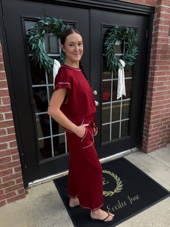 Deep red scuba lounge set with short-sleeved top, wide-leg trousers, white contrast stitching, and drawstring waist. Available in all sizes.