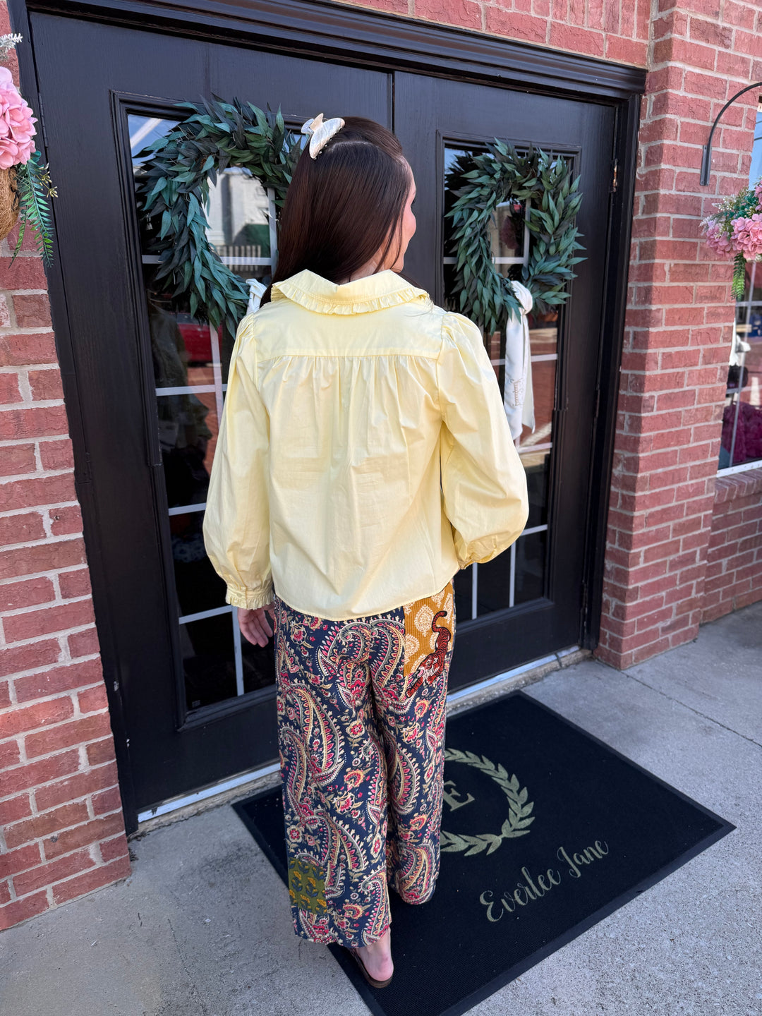 Pastel yellow collared shirt with puffed sleeves. Tiger Barrel Pant wide-leg pants in navy, red, and gold paisley print. Available in multiple sizes.