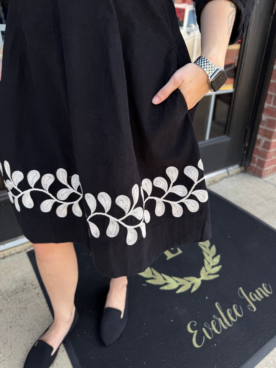 Black corduroy Vine Embroidered Dress with white vine pattern at hem and side pockets. Available in all sizes.