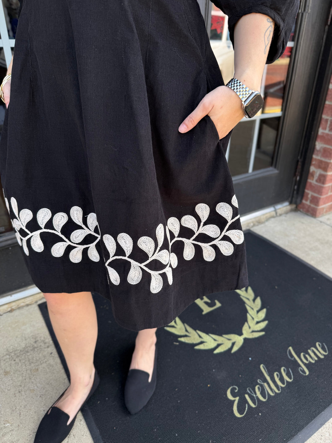 Black corduroy Vine Embroidered dress with white vine embroidery along the hem and side pockets.