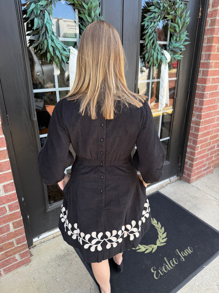 Black corduroy vine embroidered dress with button-down back, three-quarter sleeves, and cream vine hem.