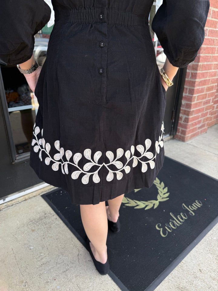 Black corduroy Vine Embroidered Dress with button-up back and white vine embroidery at the hem. Available in multiple sizes.