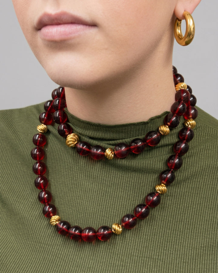 Ravello 5-in-1 Gold Necklace in cranberry, a long gold-plated piece featuring alternating translucent beads and small ridged spheres, worn doubled as an adjustable length accessory.