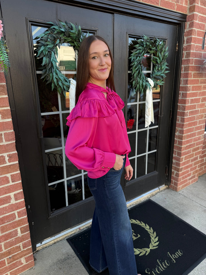 Fuchsia silky bow neck top with long sleeves and ruffled shoulders. Available in various sizes.