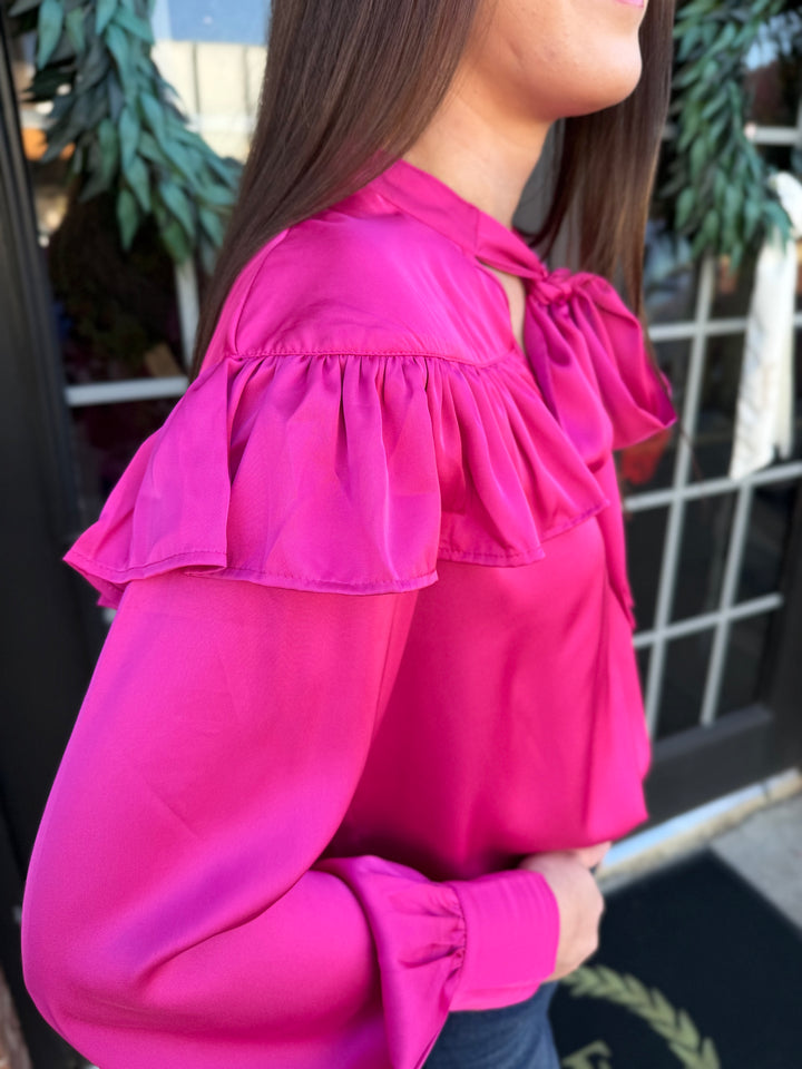 Fuchsia silky bow neck top with ruffled yoke, long sleeves, and gathered cuffs.
