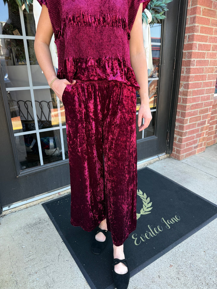 Cranberry crushed velvet wide-leg pant with a smocked waistband and side pockets.