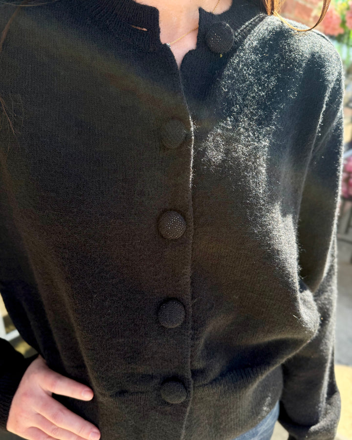 Black button-up cardigan with long sleeves, round neckline, and textured buttons. Sizes available.
