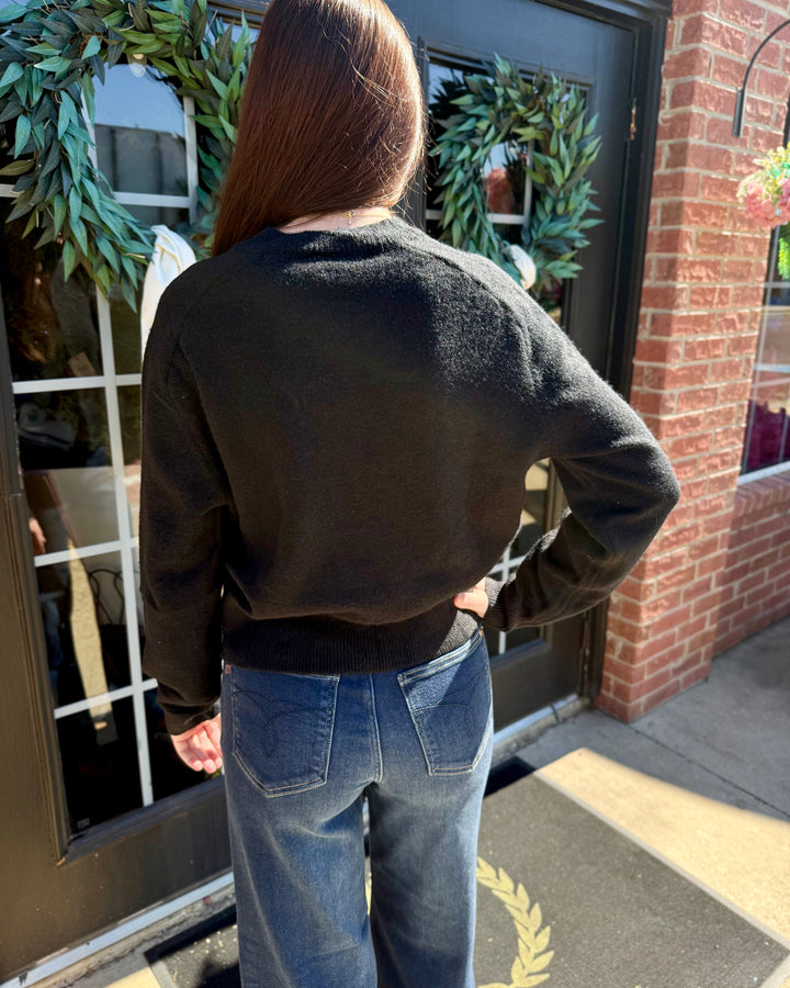 Back view of a black, long-sleeve, button-up cardigan. Available in all sizes.