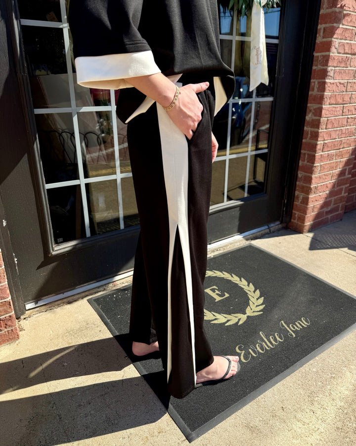 Black LuxeKnit straight pants with white side stripes and hem slits. Available in sizes XS-XL.