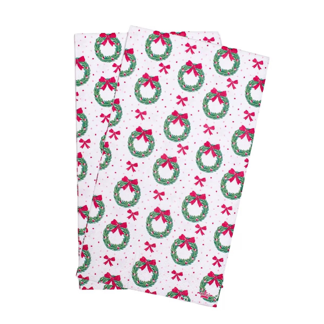 Two Clara Wreath Guest Napkins with a pattern of green holiday wreaths, red bows, and pink dots.