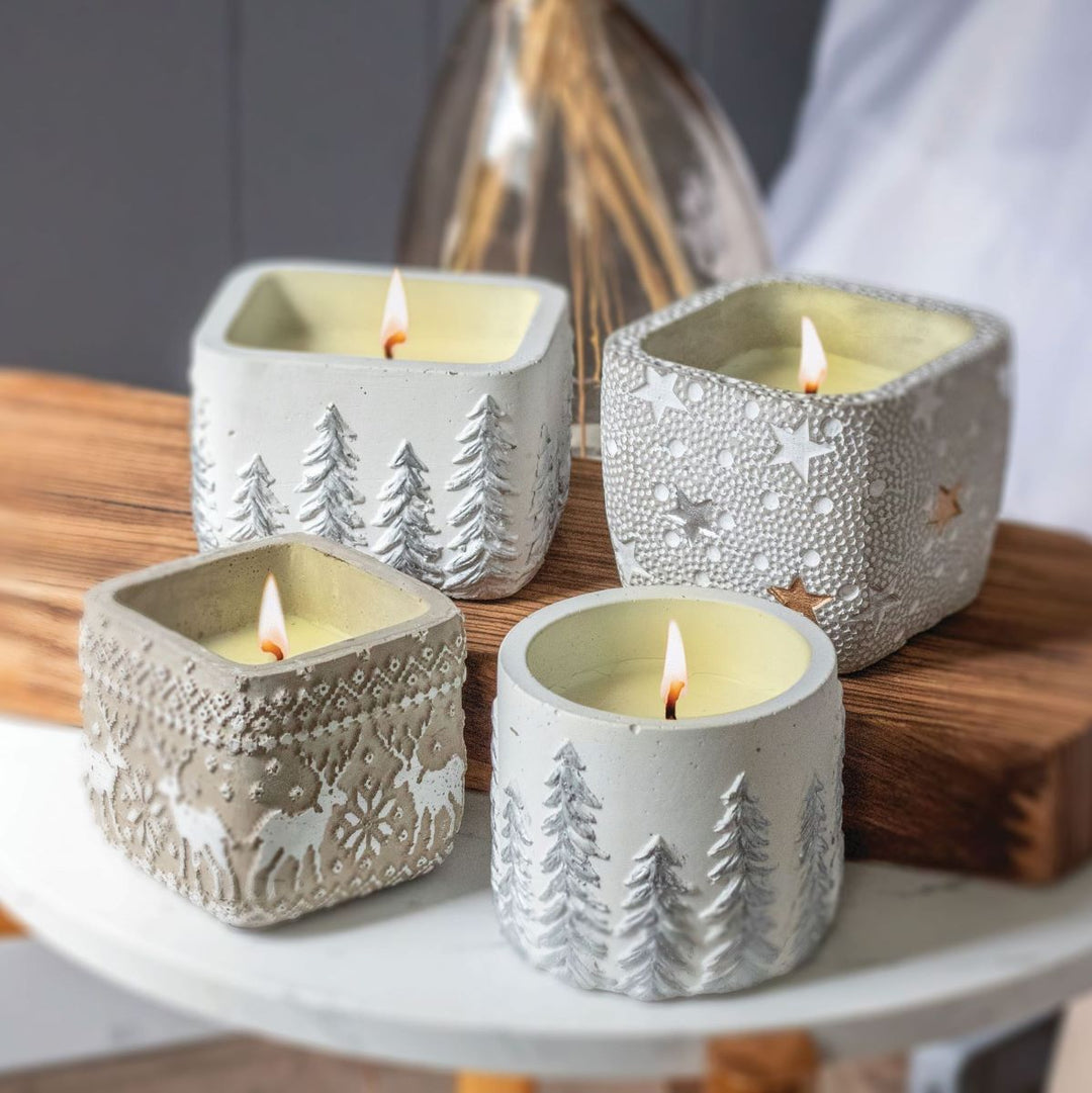 Four lit Peppermint Twist Candle in Star Pot candles in textured square and cylindrical concrete pots with embossed pine, star, and reindeer patterns.