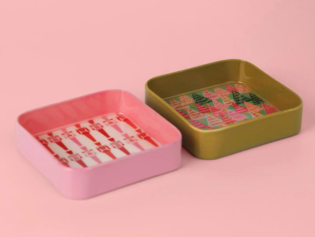 Two square Jingle Pop Dice Trays: one pink with a candy cane pattern and one olive green with a Christmas tree pattern.