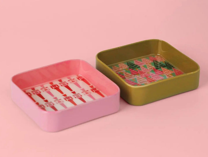 Two square Jingle Pop Dice Trays: one pink with a candy cane pattern and one olive green with a Christmas tree pattern.