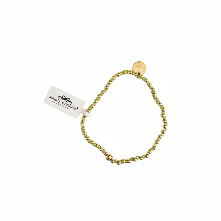 Gold beaded bracelets with green and gold accents, round gold charm, and white “simply southern” tag. Sizes: S, M, L.
