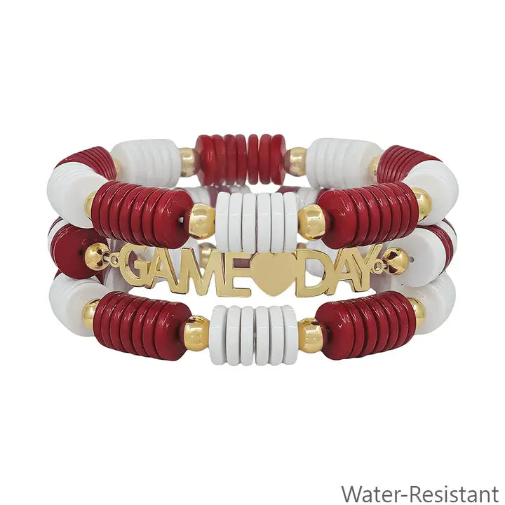 Set of water-resistant stretch bracelets with red, white, and gold beads and a gold plate engraved with “GAME DAY” and a heart. "Water-Resistant" appears in the corner. Sizes available: S, M, L.