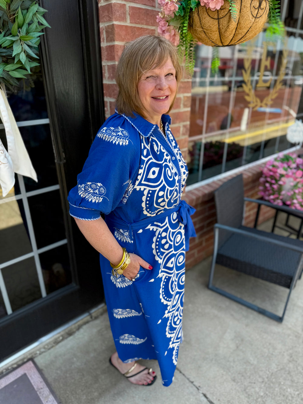 Savannah Paisley Midi Dress in blue and white paisley, features a collared V-neckline and adjustable waist tie. Available in sizes XS–XL.