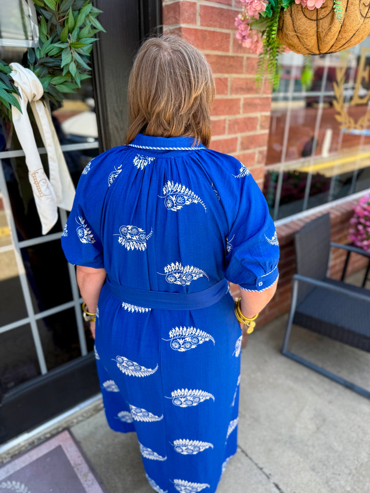 Savannah Paisley Midi Dress with a blue base, white paisley patterns, and adjustable waist tie. Available in sizes XS–XL.